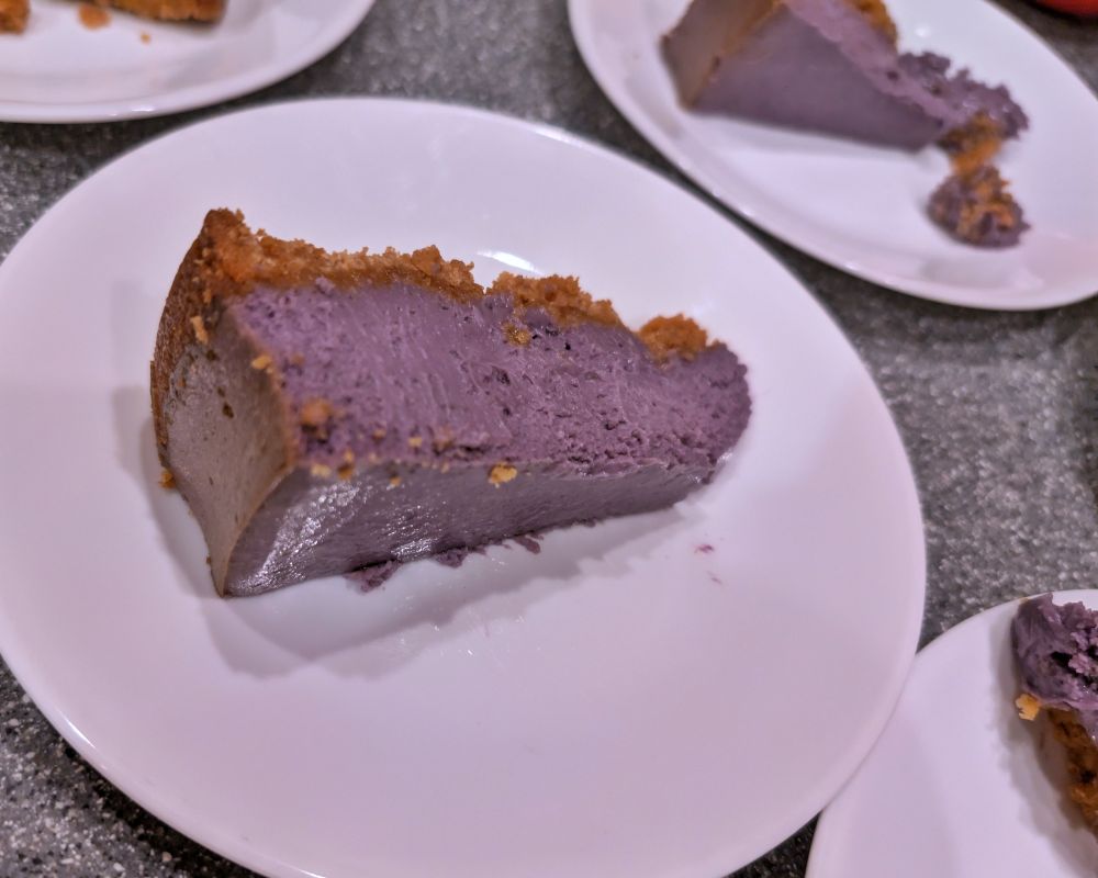 Several plates of purple ube cheesecakes with graham cracker crust on white plates 