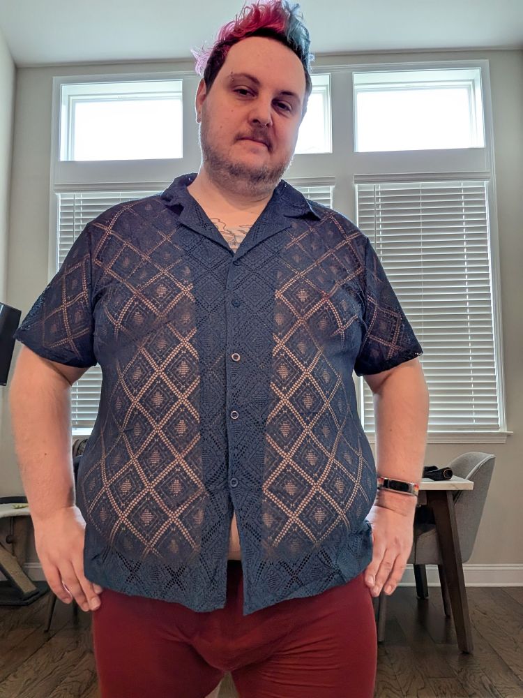 A chubby white person in a navy colored knit button down shirt. The knit has lots of gaps allowing the skin under the shirt to be visible. The shirt peaks open at the bottom due to the persons large belly and the positioning of the buttons. They also have dark red underwear on. 