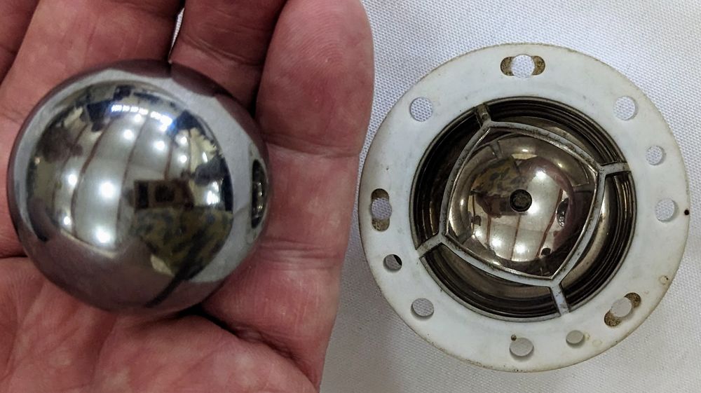 An actual (hollow) beryllium sphere sitting in my hand, next to a half of the thing that contained it.  