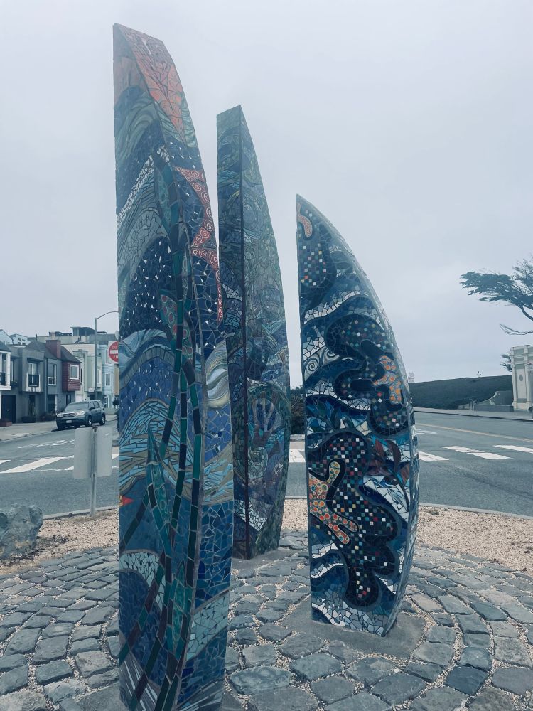 Colorful mosaic sculptures with appearance of sails or surfboards grazing part of a neighborhood near the ocean. 
