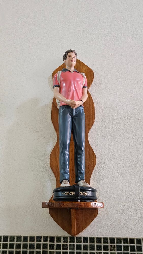 Foto de uma pequena escultura, tipo imagem de santo católico, de Carlo Acutis, o santo millennial