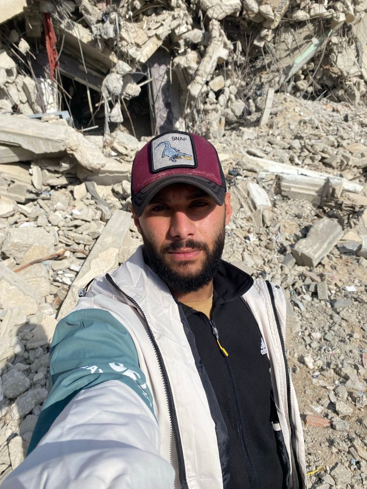 A young man in Gaza stands amid the ruins of destroyed buildings, taking a selfie with a serious expression.
The rubble around him tells the story of war, hunger, and survival he is alive, but surrounded by the remains of everything he once knew.