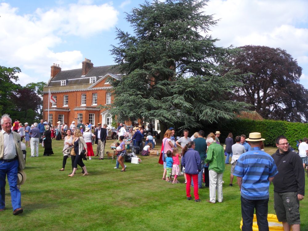 Lots of people milling around on a lawn before a manor house