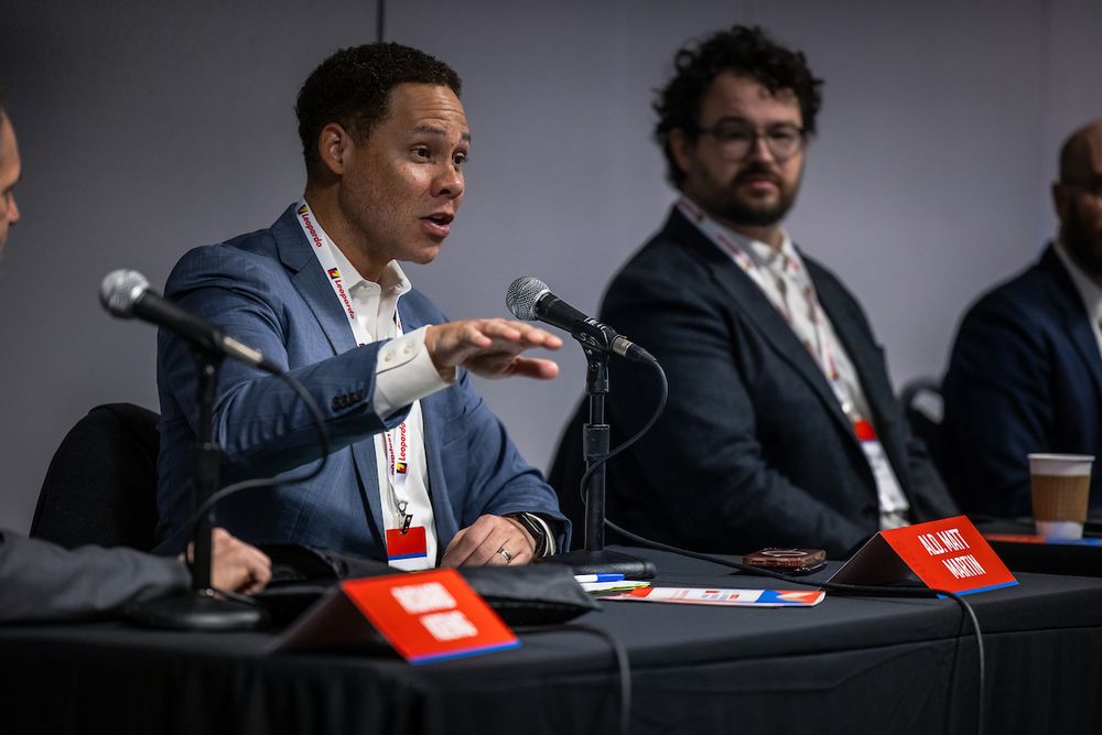 Alderman Matt Martin in a blue jacket holding his hand up speaks into a microphone next to Daniel Kay Hertz in a black jacket listening during the Navigating NIMBYism: Legal and Policy Strategies for Affordable Housing Development panel at the IHC Conference in Chicago in February 2025.