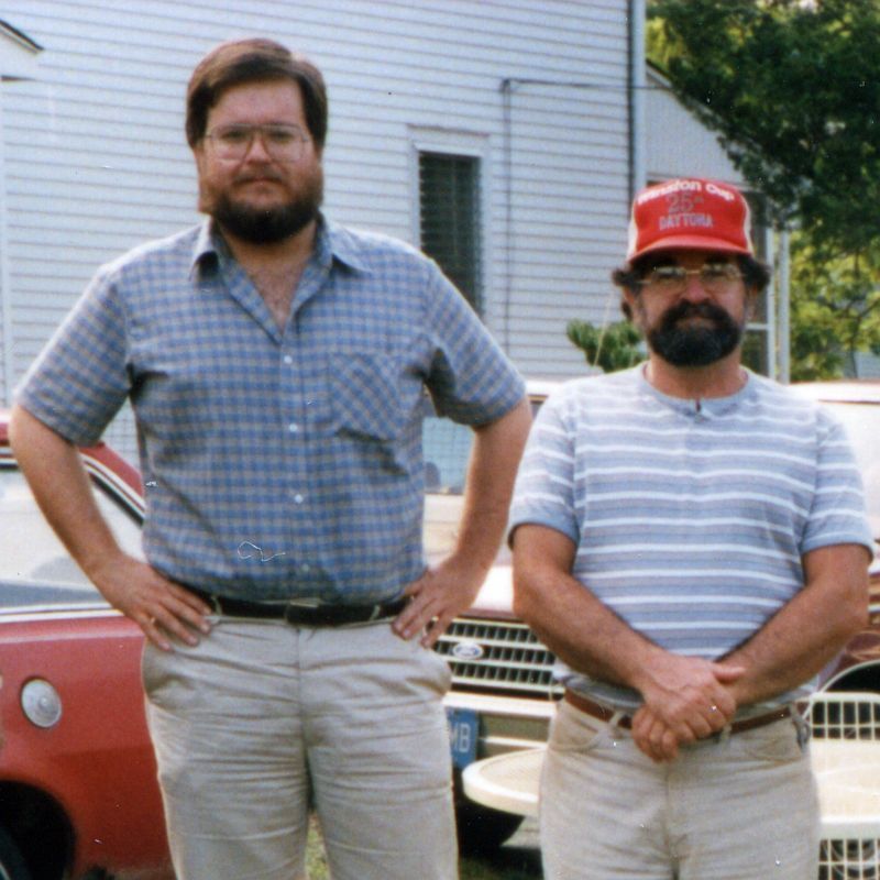 Photograph of David Milley and Warren Davy, taken in the late 1980s, standing side-by-side in the side yard of their house.