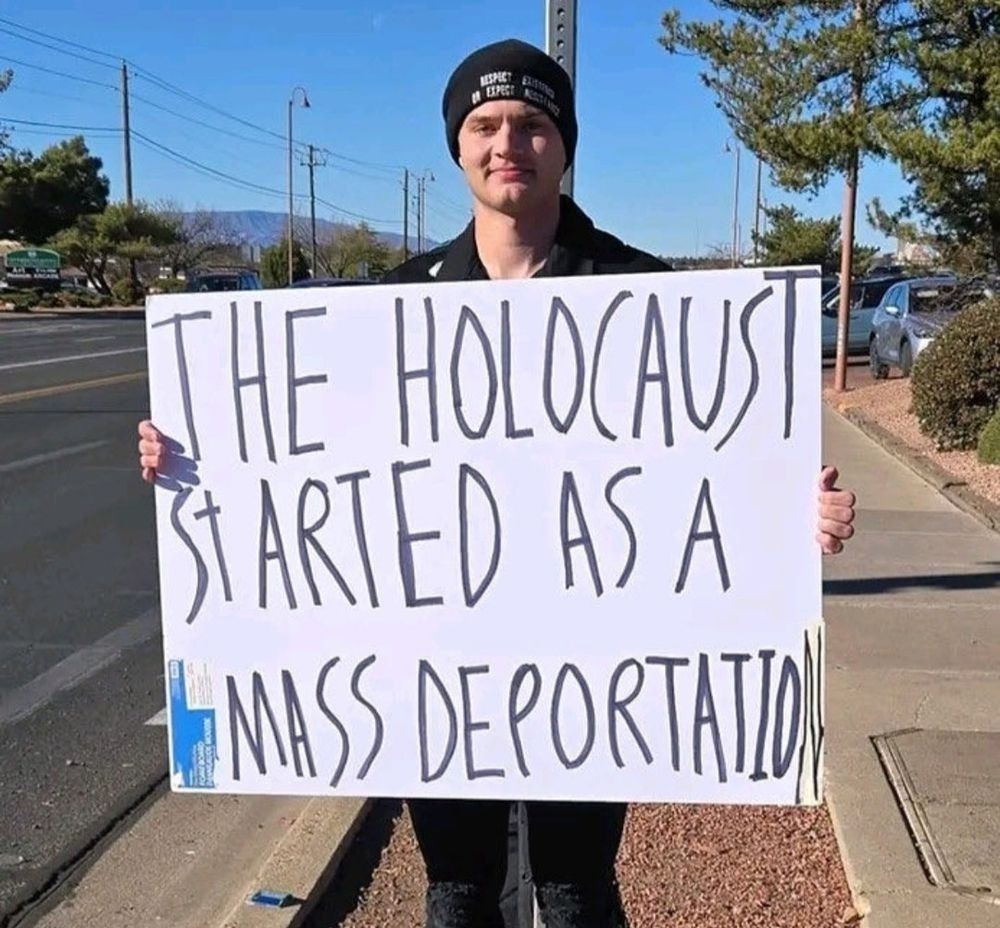A man holding a sign that reads, "The Holocaust started as a mass deportation."