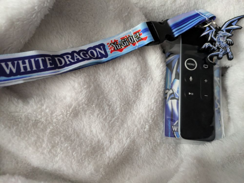 Apple TV remote on a Yu-Gi-Oh! Blue Eyes White Dragon (Seto Kaiba merch) lanyard.