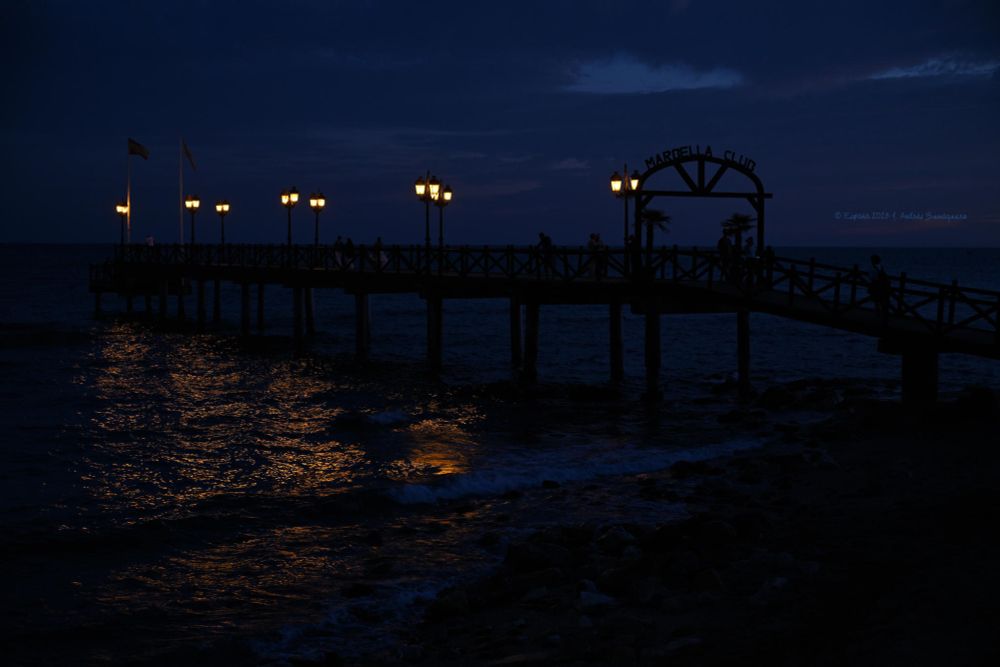 Una imagen cuando llega la noche y en el embarcadero quedan iluminadas sus farolas, cuyos reflejo se ven dorados en el mar.