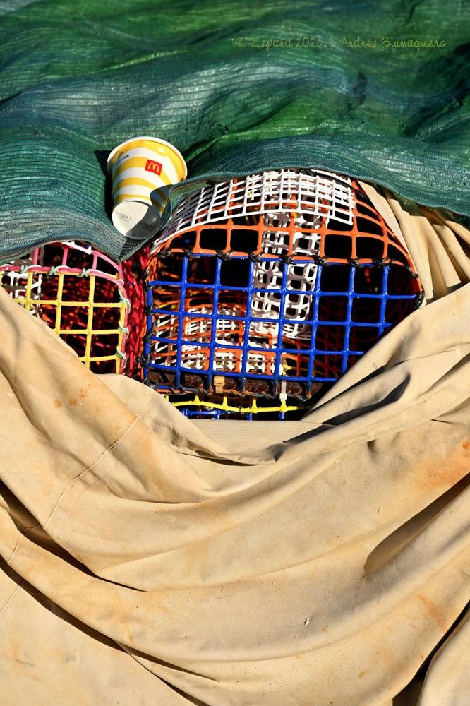 Una lona verde y otra beis claro dejan entrever por un hueco una par de nasas. Hay también un vaso de refresco sobre la lona verde.