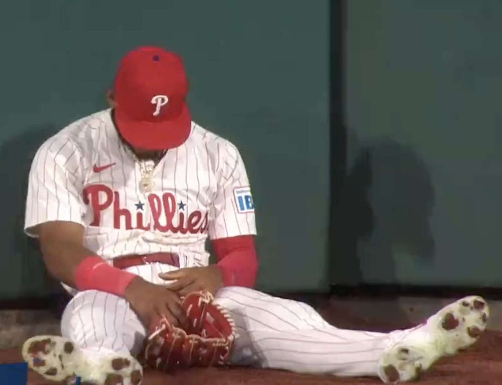 Sad looking Phillies player. His red hat is covering his face. His glove is off his hand and on the ground