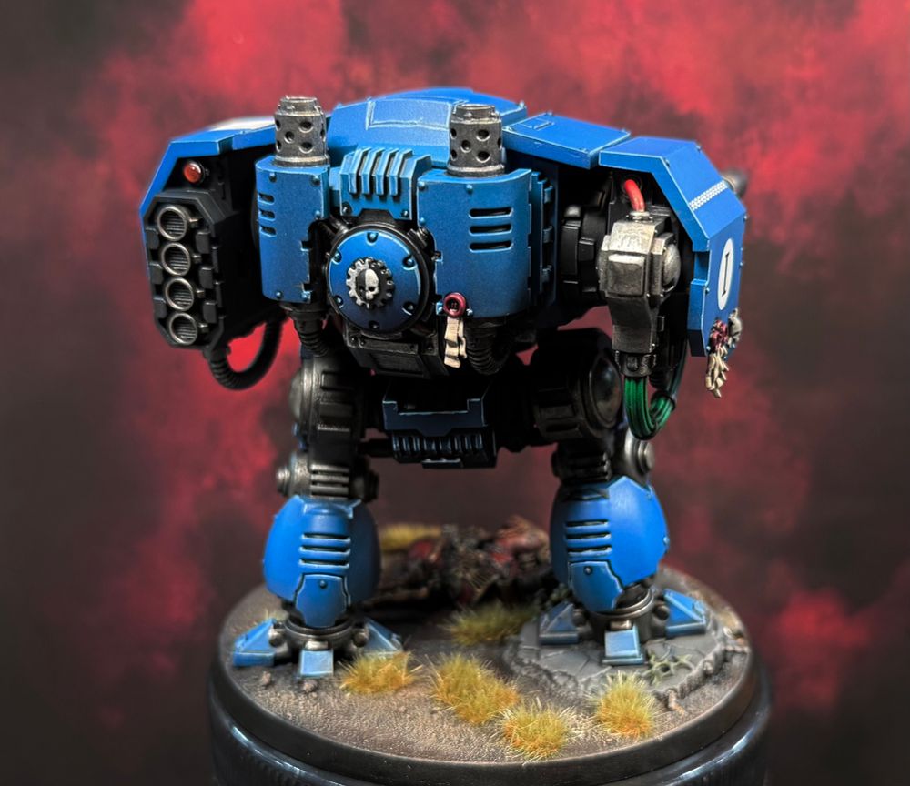 Rear shot of the badonkadonk of this big blue Ballistus Dreadnought. The symbol of the Mechanicus is proudly displayed between its exhaust stacks. You can also see the bright green power cabling for the starboard lascannon. 
