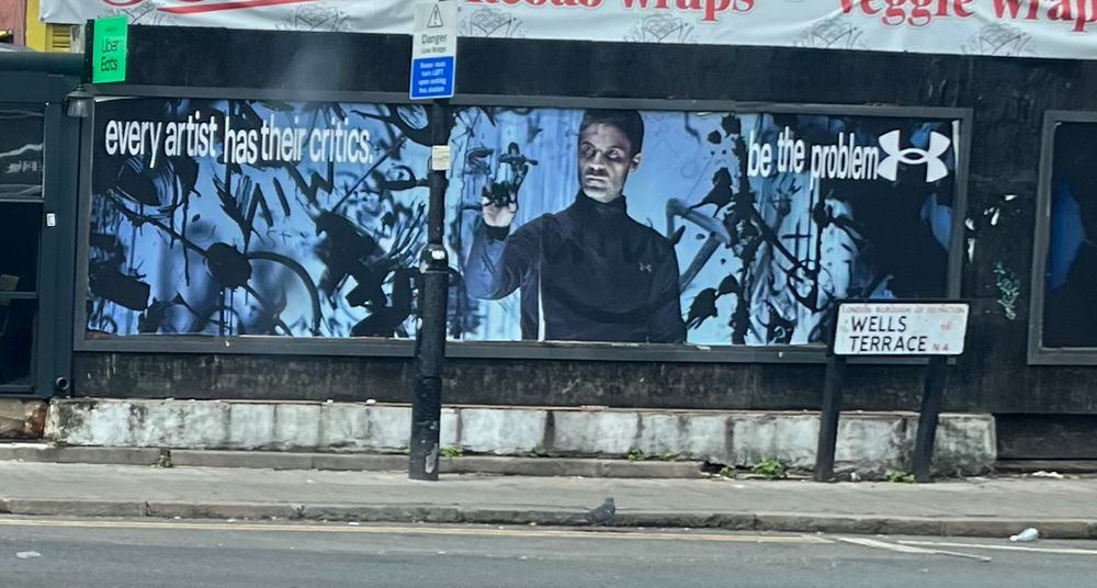 Poster on a wall that reads “every artist has their critics. be the problem”