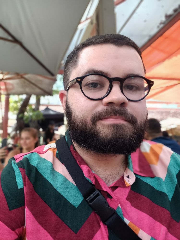 Homem branco de barba e óculos com uma camisa colorida 
