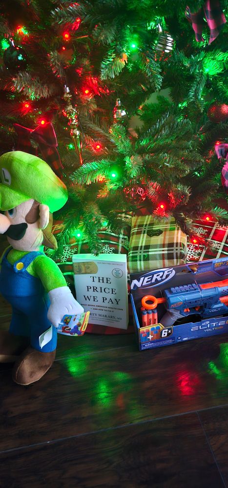 Presents under lit christmas tree left to right: Stuff Nintendo Luigi plush, book "The Price We Pay: What Broke American Health Care and how to Fix it", nerf gun with "deny, defend, depose" written on darts.