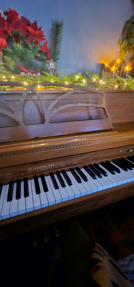 Upright walnut Baldwin piano with pine garland and candles lit with white light. Poinsettia flowers.