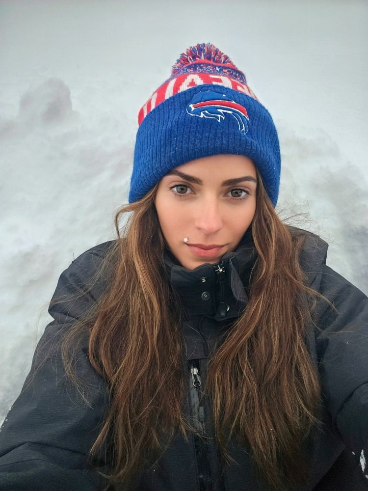 Myself (woman, long brown hair, Buffalo Bills winter hat and black ski jacket) sitting in three feet of snow 