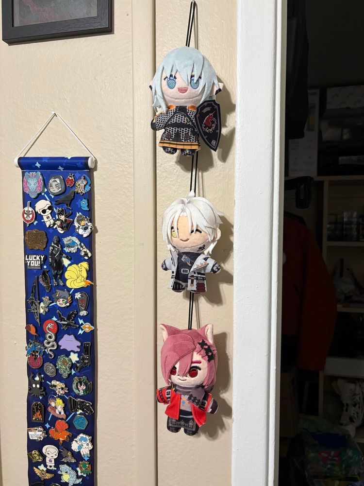 photograph of my wall decorations; in center frame are three plushies - from top to bottom, haurchefant, thancred and graha tia - all made by chibidachi. theyre all very cute
