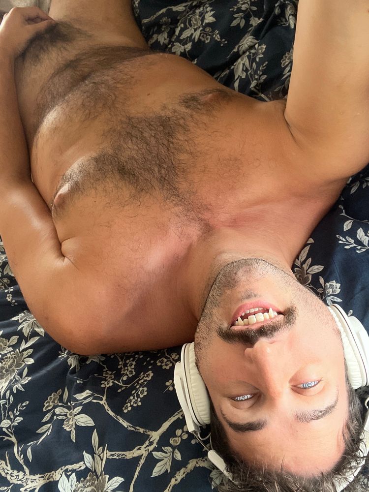 Dano laying down with spirals in his eyes and enhanced canine teeth. He wears headphones and one hand gently touches his crotch 