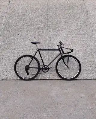 A black bike leaned against a wall. the rear tire isn't close to the seat tube, and it has a carrier over the front wheel.