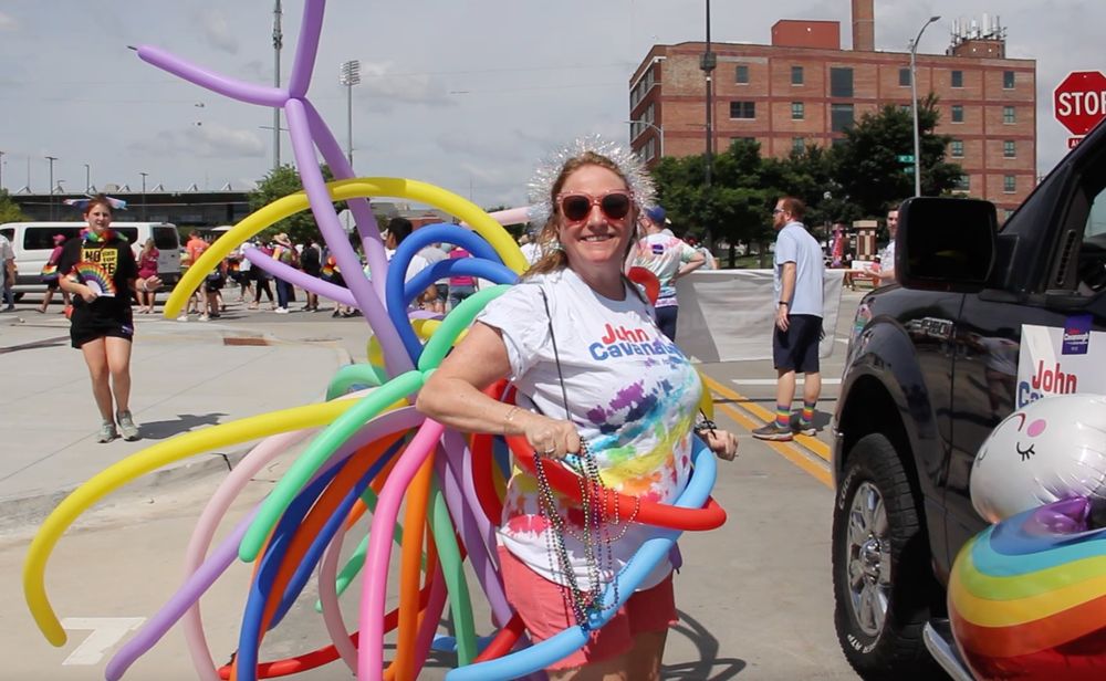 A woman in a tie dyed T-shirt wears rainbow balloons. 