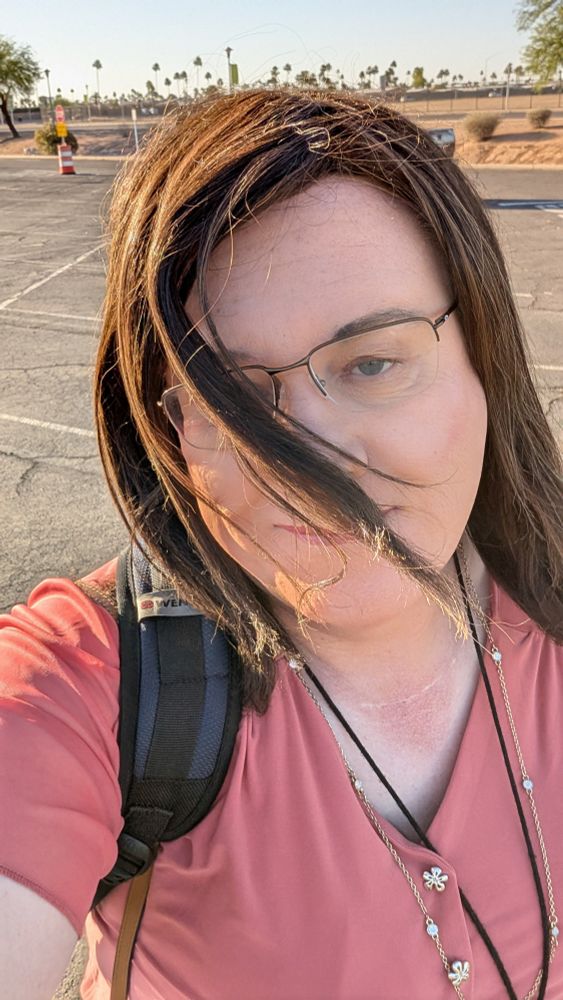 Early morning picture of me wearing a peach top, walking in a parking lot.  Wind blowing hair into my face.