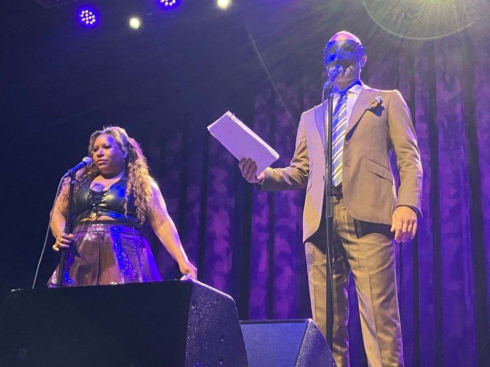 Symphony Sanders and Cecil Baldwin perform on stage. Cecil is wearing a crow beak mask with feathers around the eyes. 