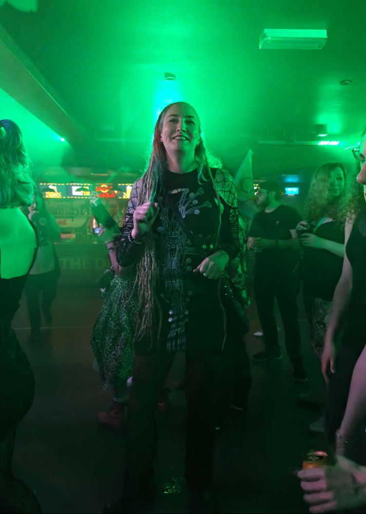 Lisa wearing a bodycon dress with wiring on it in the shape of a cross, and fishnet on her arms and shoulders.  Picture taken in a nightclub with a bright green light behind her giving her an aura.  Thats right. My aura was green last night.  