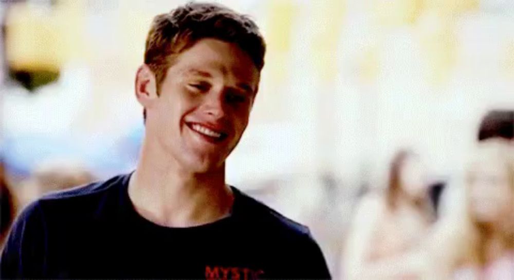 a young man in a black shirt is smiling while standing in front of a crowd of people .