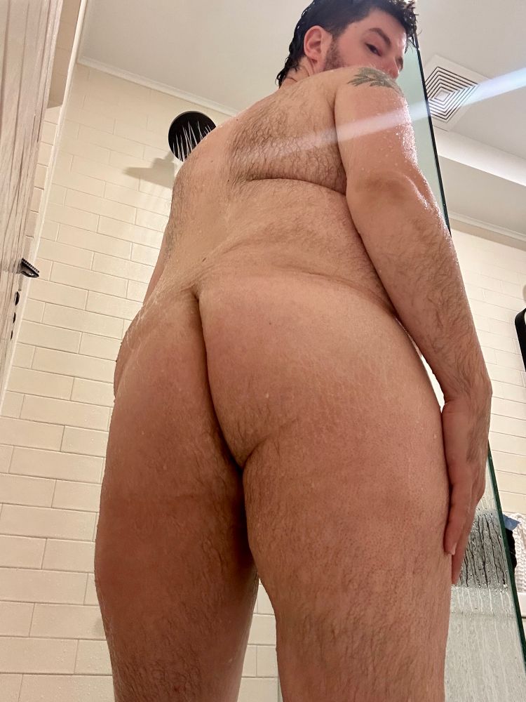 Bstnbear nude in the shower with his back and butt to the camera, looking over his shoulder. 