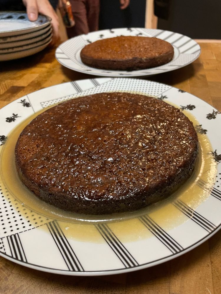 Whole sticky toffee pudding resting in a pool of caramel sauce 