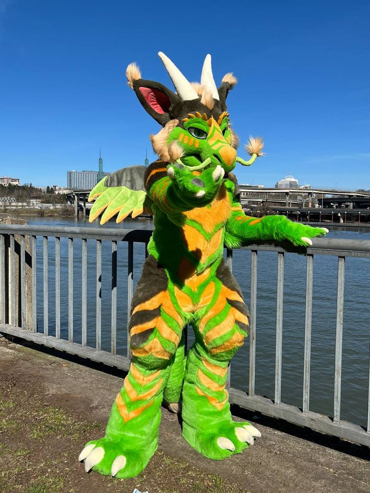 Fursuit of Rathtolar leaning on a railing next to a river