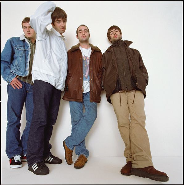 Oasis, photographed at Perseverance Studios, East London. 1995. The band members are all posing, lined up against a white background.
From left to right: Alan White, Noel Gallagher, Bonehead, Liam Gallagher. Guigsy is not pictured.

White has his hand placed on his hip. Next to him, Noel has a hand on the top of his head as if he was scratching it. Bonehead is posed with his hands in his pockets, one leg crossed over the other. Liam is leaning against the wall with his hands in his pockets.