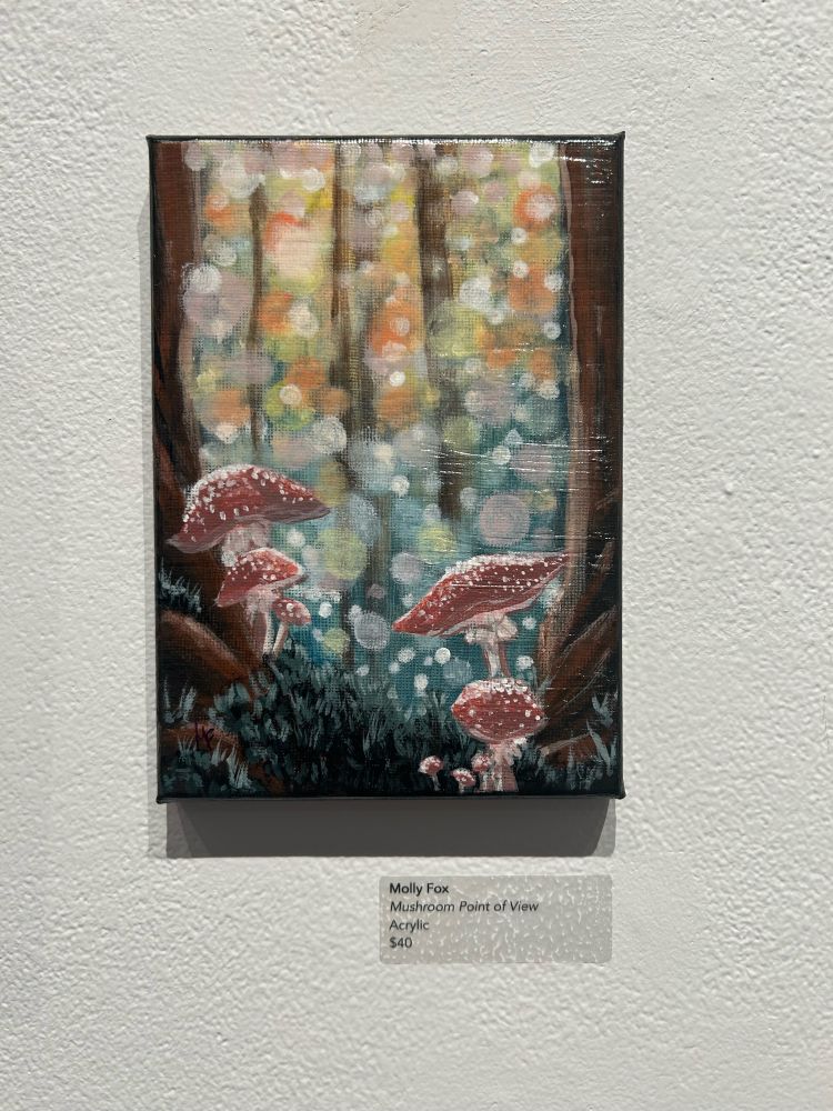 Mushroom point of view painting hung in the gallery with my information card. Red mushrooms with white spots nestled between roots and trees, with an out of focused background 