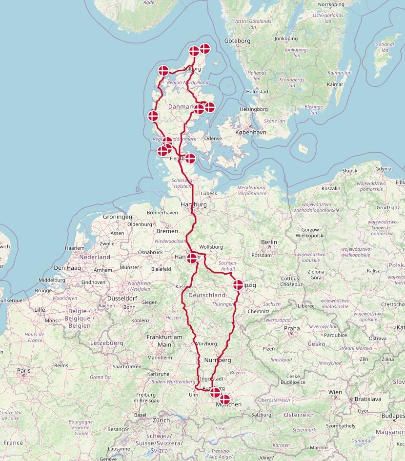 Screenshot aus OSM mit einer Roten Linie, die unsere Fahrtroute vom Hannes Camper Depot in Puchheim bis nach Skagen und zurück repräsentiert. Die wichtigsten Punkte sind mit Kreisen mit der Dänemark-Flagge gekennzeichnet.
