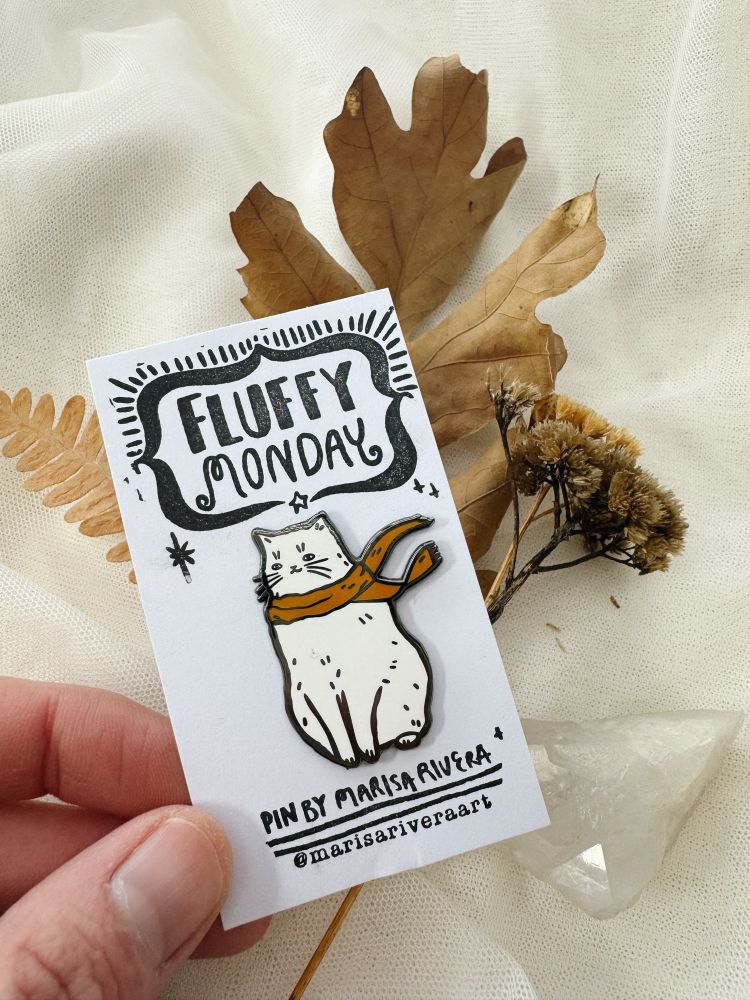 White enamel pin of a cat wearing an orange scarf with a fluffed coat because the cold wind is blowing
