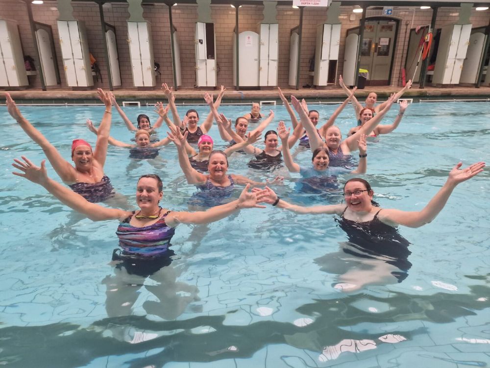 women and non binary  swimmers with arms in air smiling