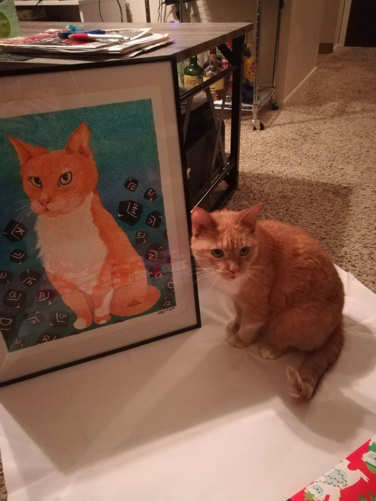 Caps Lock staring, seated next to the framed portrait of Caps Lock, a drawing showing the cat surrounded by keyboard keys