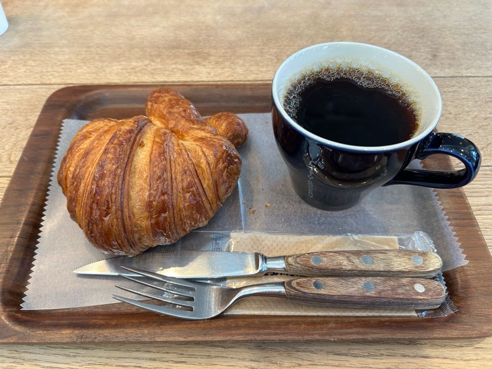 木のトレイにのったクロワッサンとコーヒーが映っている