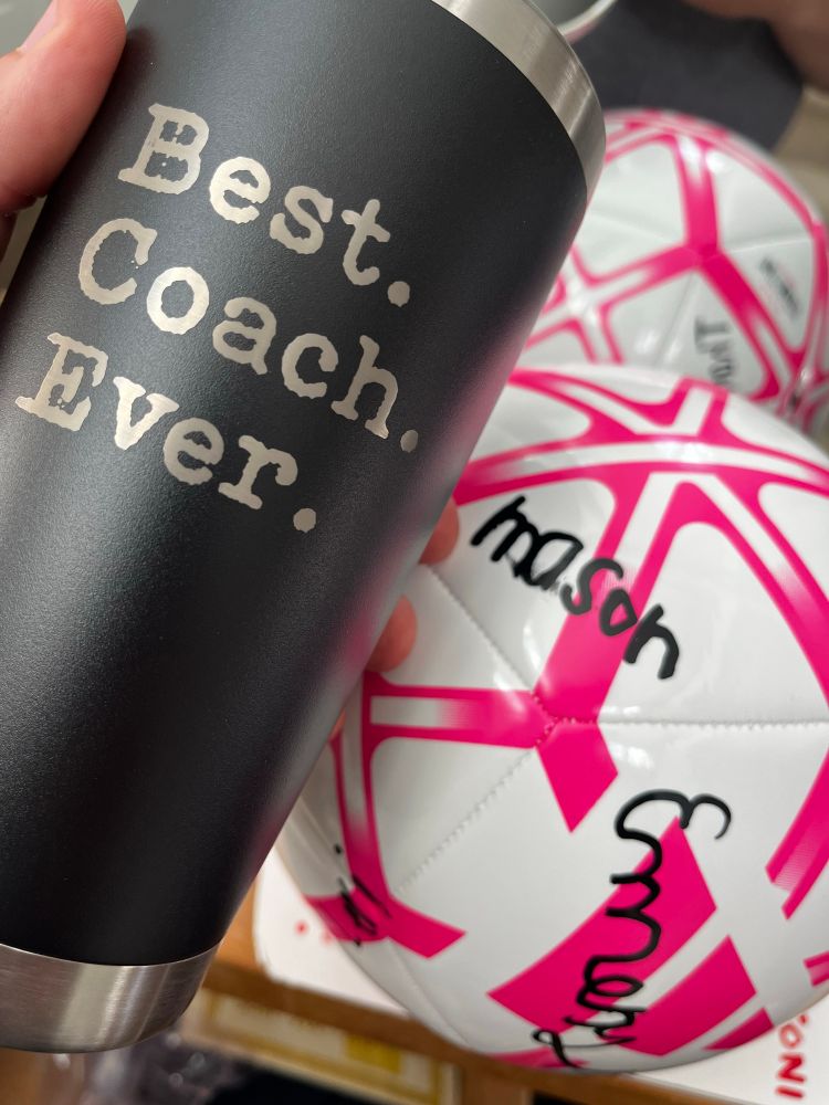 Two gifts from the team: A black stainless steel tumbler that says “Best Coach Ever” and a pink soccer ball that all the players signed.