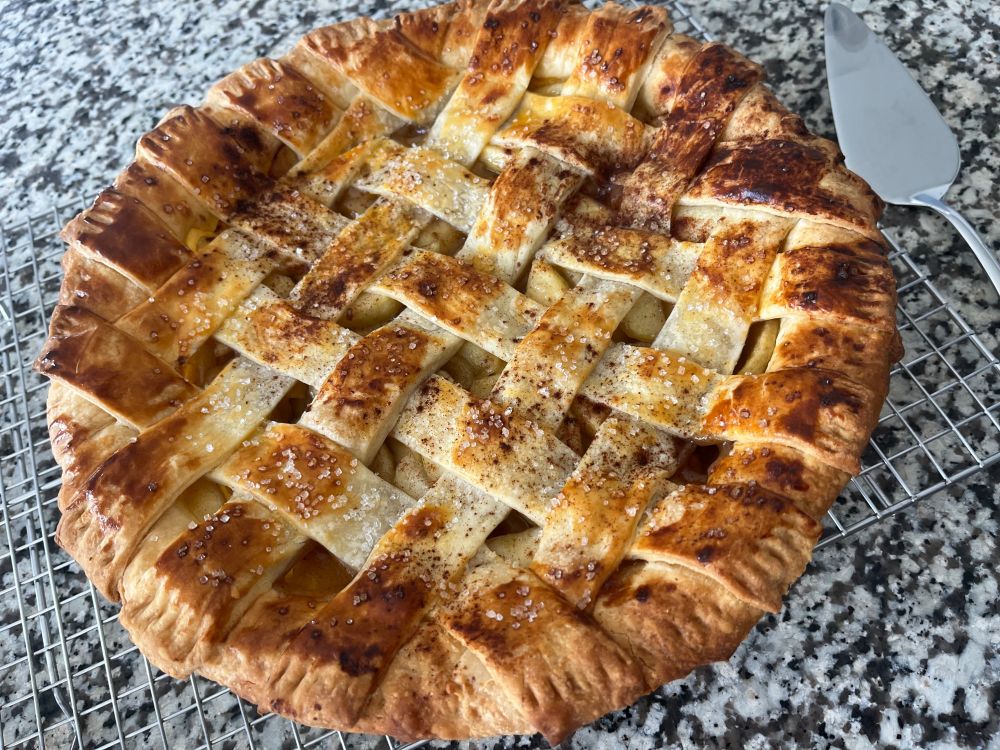 A golden brown apple pie cooling on a wire rack. The top crust is an overlapping lattice.