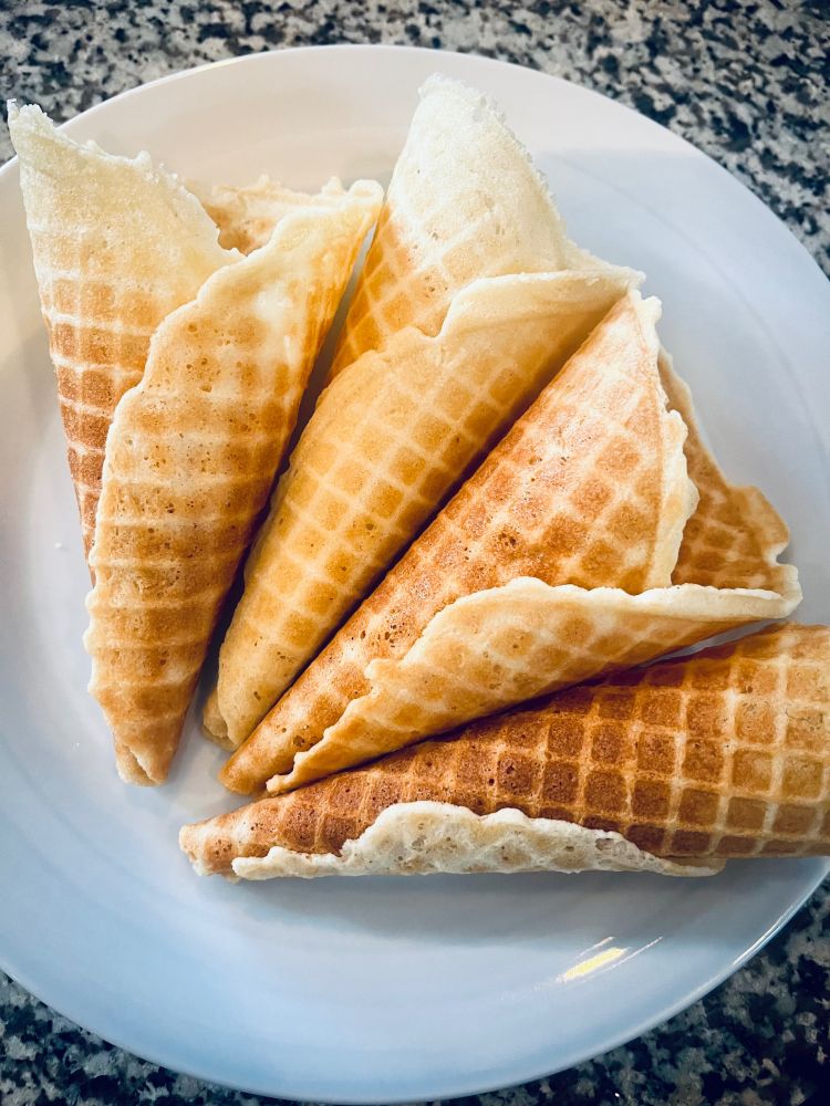 Four golden brown ice cream cones resting on a plate.