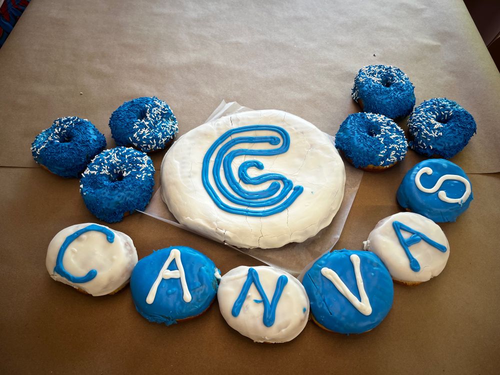 An assortment of blue and white frosted donuts that spell out “CANVAS,” and a giant donut cake with the design system logo “C” on it.