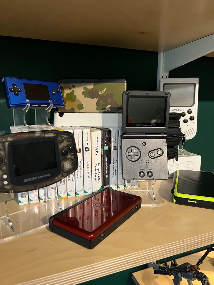 A few old Nintendo handhelds on a shelf. Gameboy advanced, SP, micro, DS lite, and a 3DS. 