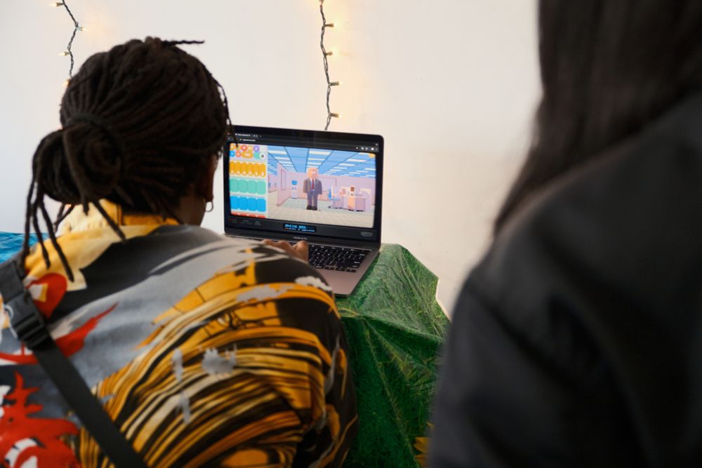 Photo of the back of an attendee playing a game in a laptop. The game appears to be in a corporate setting, within a 3d environment.