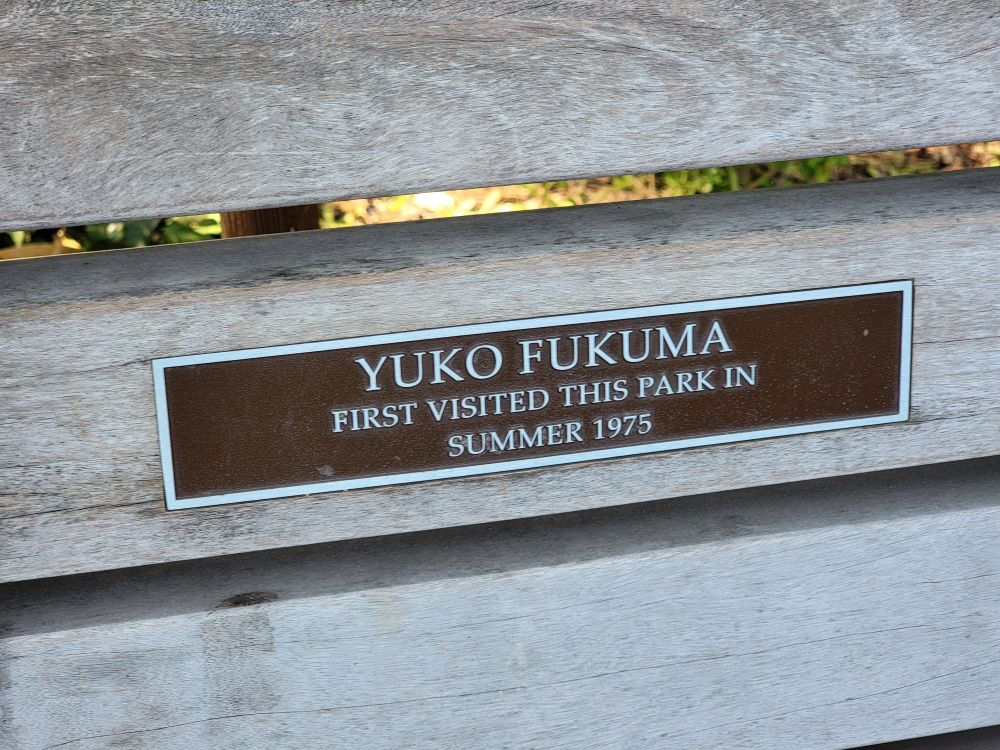 Commemorative metal plaque on the wooden "Happy to chat" bench in Central Park reads: "Yuko Fukuma first visited this park in Summer 1975."