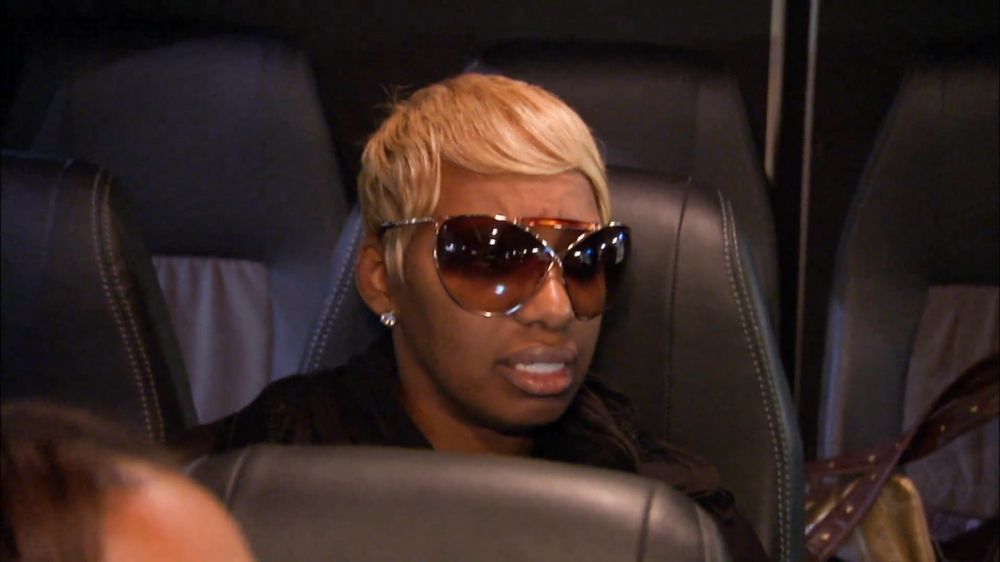 A woman sitting in a airplane or bus seat wearing oversized sunglasses making a distressed face 
