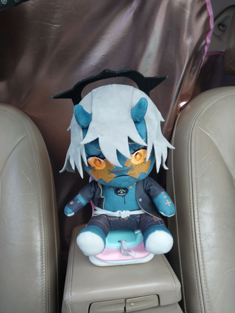 goodsmile happy chaos plushie sitting in a small booster seat (meant for smaller plushies) buckled in. he is ready. sort of.