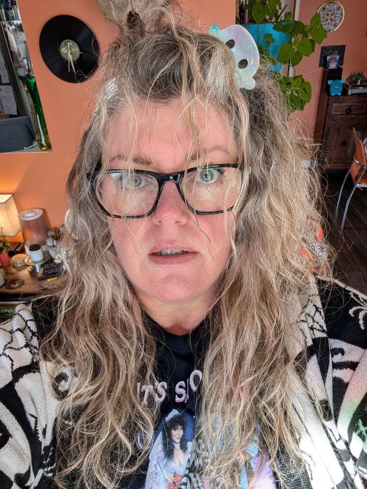 A woman with past shoulder length wavy blonde and gray hair, is wearing a ghost hair clip. The hair is over her face and she's very red in the face because she's been out in the cold