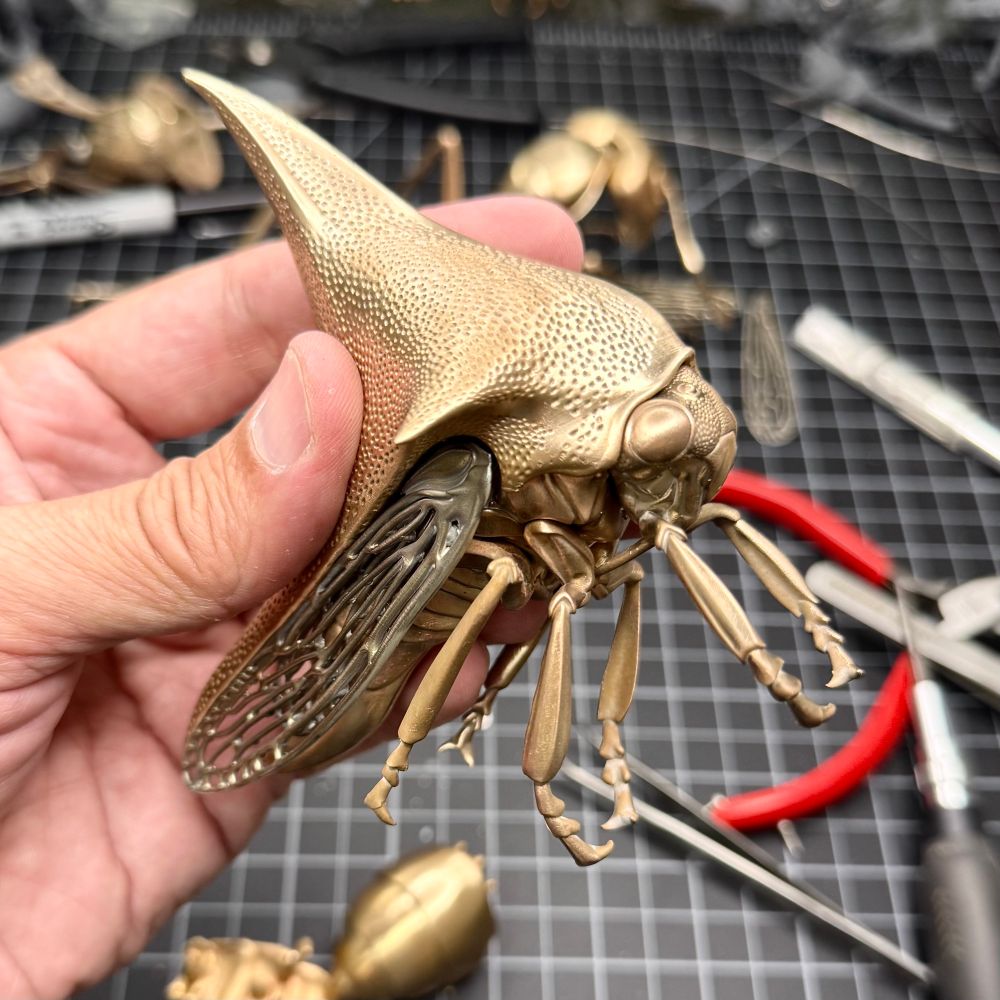 The assembled Thor bug held in my left hand above a crowded workbench. The bug is extremely detailed, particularly underneath.