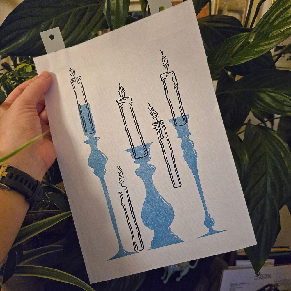 Photo of a hand holding an in progress linocut print of candles in glass holders, all blue